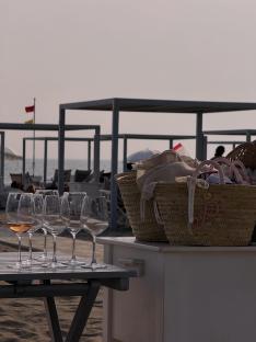 Wine glasses on a table next to wicker baskets on a beach.