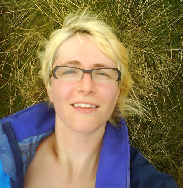 Woman lying in grass wearing glasses and a jacket.