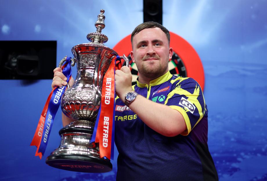 Luke Littler holding the Phil Taylor Trophy.