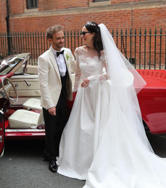 Newlyweds exiting a red Mustang convertible.