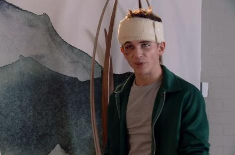 A young man with a head bandage speaks.
