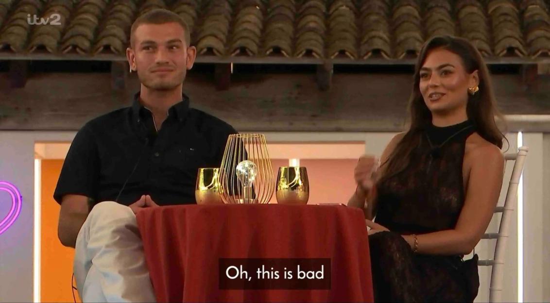 Screenshot of a man and woman sitting at a table during a conversation.