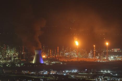 Smoke and flames rise from an oil refinery at night.