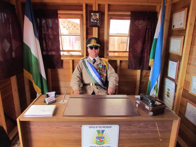A man in military uniform sits at a desk in the presidential office of the Republic of Molossia.