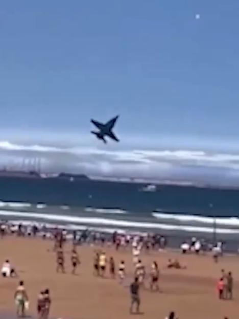 Jet plane flying low over a crowded beach.