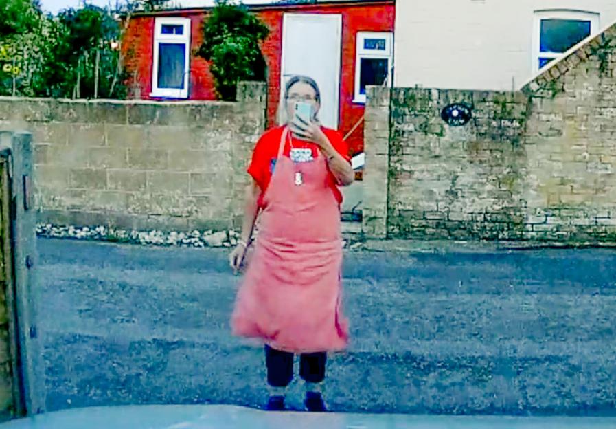 Woman in red shirt and pink apron holding a phone.