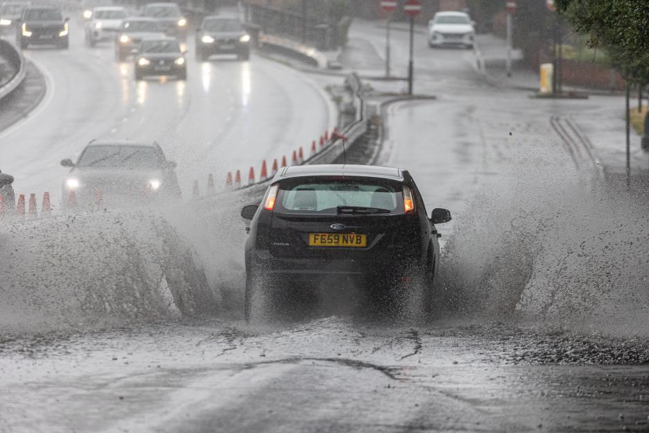 Car splashing through deep water on a flooded road.