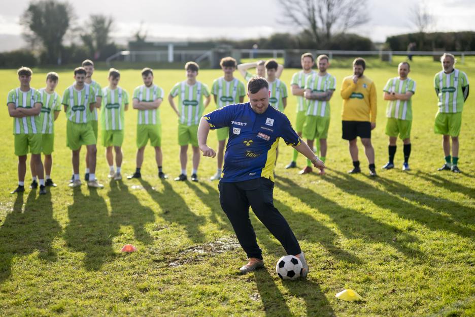 A man practices soccer in front of a team.