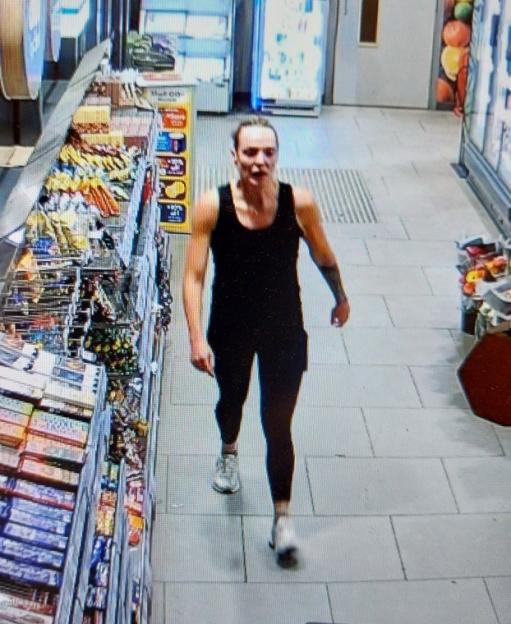 CCTV image of a woman in a black tank top and leggings, walking in a store.