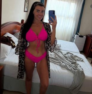 Woman in pink bikini and leopard-print robe taking a selfie in a hotel room.