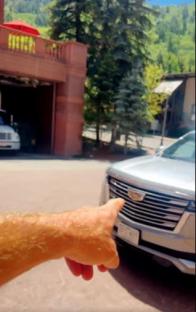 Hand pointing at a silver Cadillac Escalade.