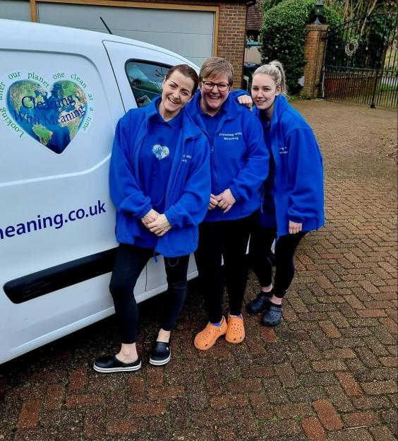 Three women in blue uniforms stand by a van with a 