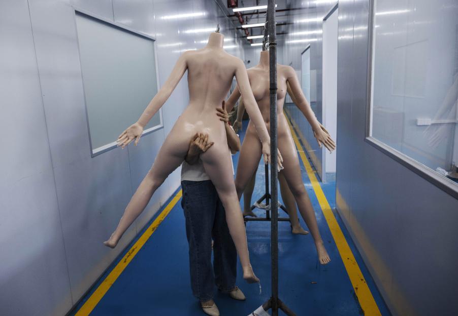 Photo of a worker carrying a silicone sex doll in a factory.