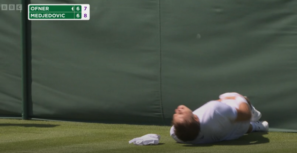 Tennis player lying on the court in pain. Scoreboard shows Ofner 6-7, Medjedovic 6-8.