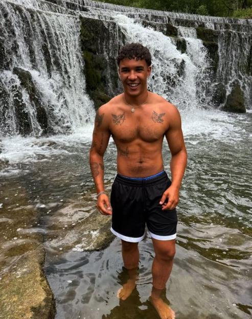 Man standing in shallow water in front of a waterfall.