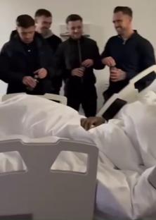 Four men visiting a person in a hospital bed.