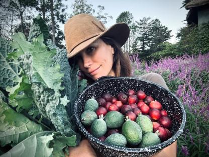 Woman holding kale and a bowl of feijoas and other fruit.