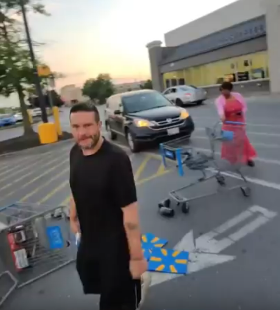 Man standing in a parking lot with overturned shopping carts and a woman walking away.