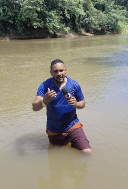 Reporter in river, holding microphone, appearing to have touched something underwater.