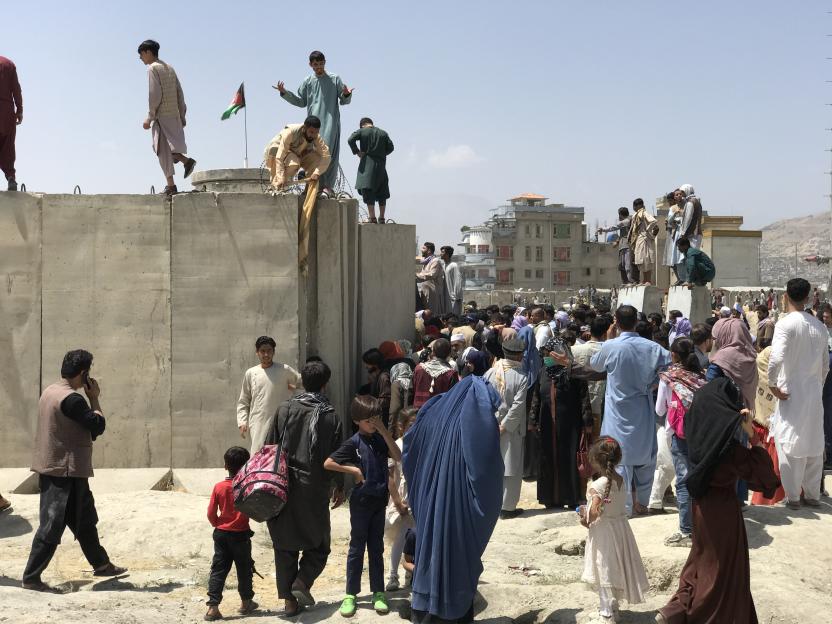 People struggle to cross a boundary wall at Hamid Karzai International Airport.