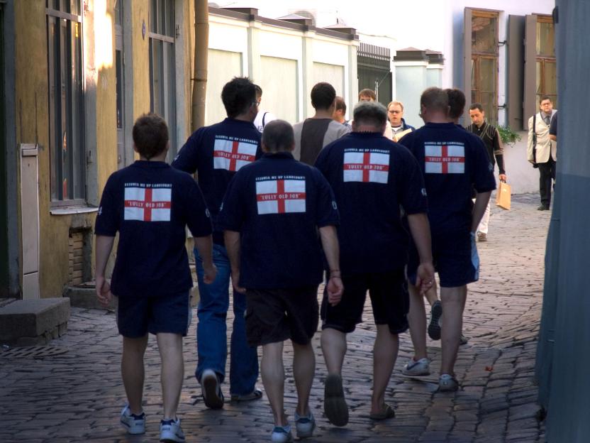 Group of men wearing matching shirts with an English flag and text walking down a cobblestone street.