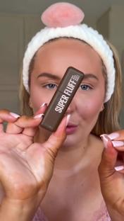 Woman holding up a tube of brow mousse.
