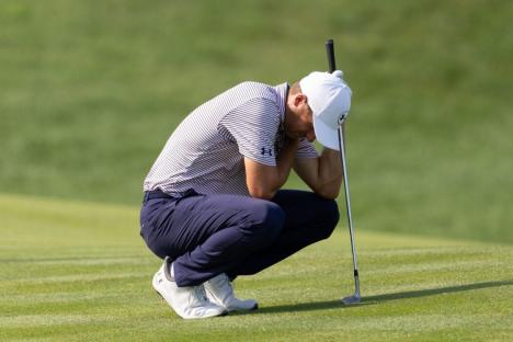 Golfer crouching on the green, head in hands, near his club.