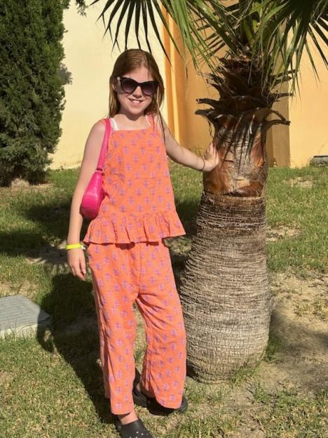 Girl in orange patterned pants and top standing next to a palm tree.