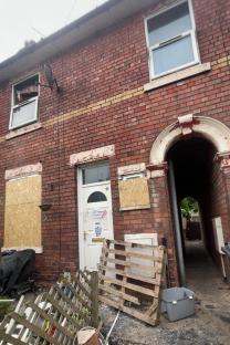 Fire-damaged terraced house with boarded-up windows.