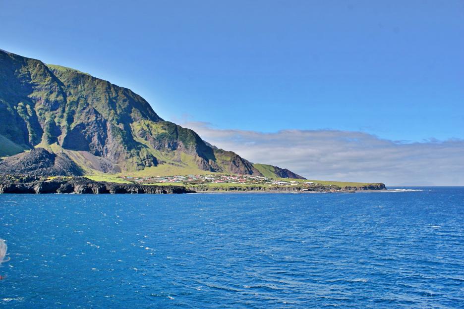 Remote island with a village nestled at the base of a steep, green mountain.