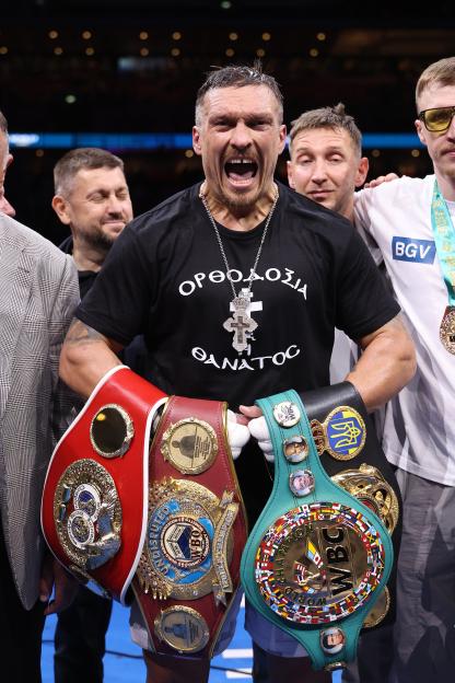 Oleksandr Usyk holding four world heavyweight championship belts after a boxing match.