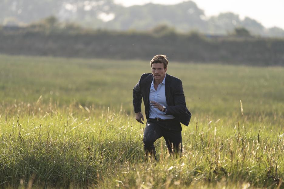 Man in suit running through tall grass.