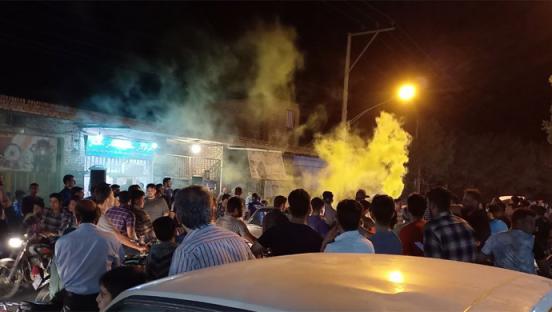 Large crowd of people at night with green and yellow smoke in the air.