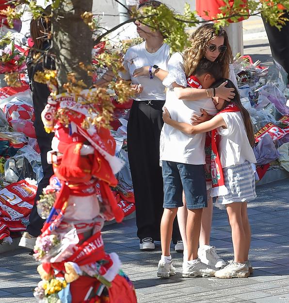 Woman and children embracing at a memorial with Liverpool scarves and flowers.
