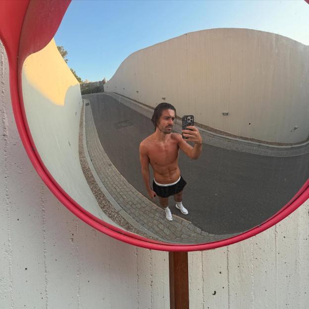 Reflection of shirtless man taking a selfie in a curved mirror.