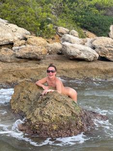 Woman sunbathing nude on rocks in the ocean.