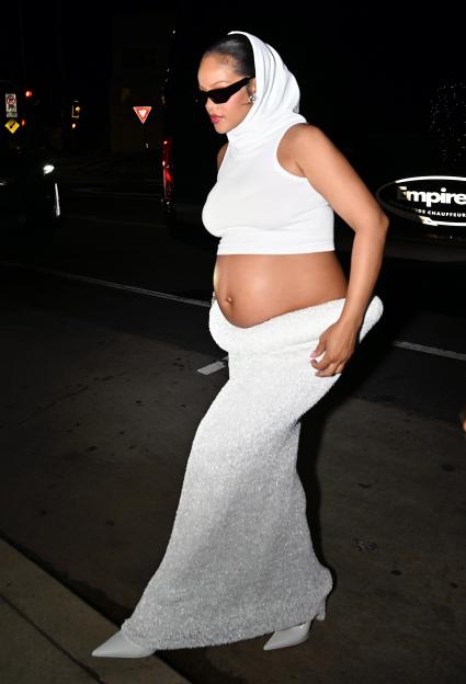 Rihanna wearing a white hooded top and long white skirt, showing her baby bump.