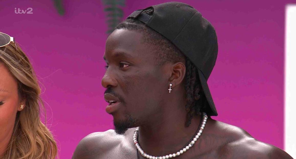 Close-up of a man from Love Island wearing a black baseball cap and pearl necklace.
