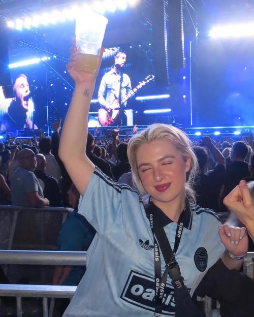 Woman at an Oasis concert holding up a drink.