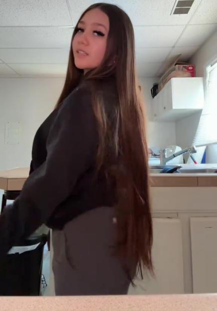 Woman with long brown hair in a black sweater and gray pants.
