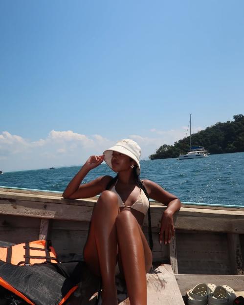 Woman in a bucket hat and bikini sitting on a boat.