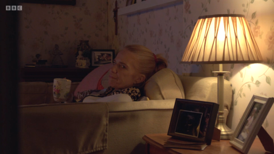 A woman relaxing on a sofa with a mug, illuminated by a table lamp.