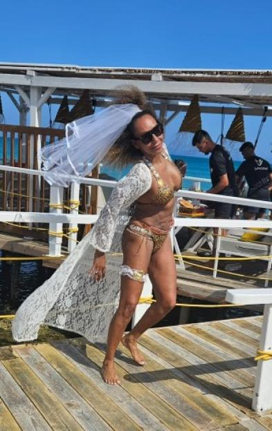 Mel B at a hen party, wearing a white lace robe and gold bikini.