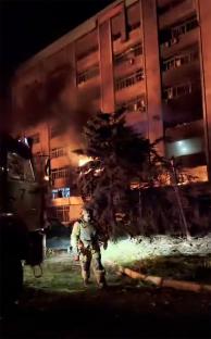 A burning building at night, with a first responder walking in the foreground.