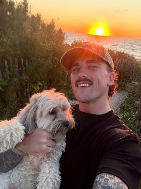 Man holding a small fluffy dog at sunset.