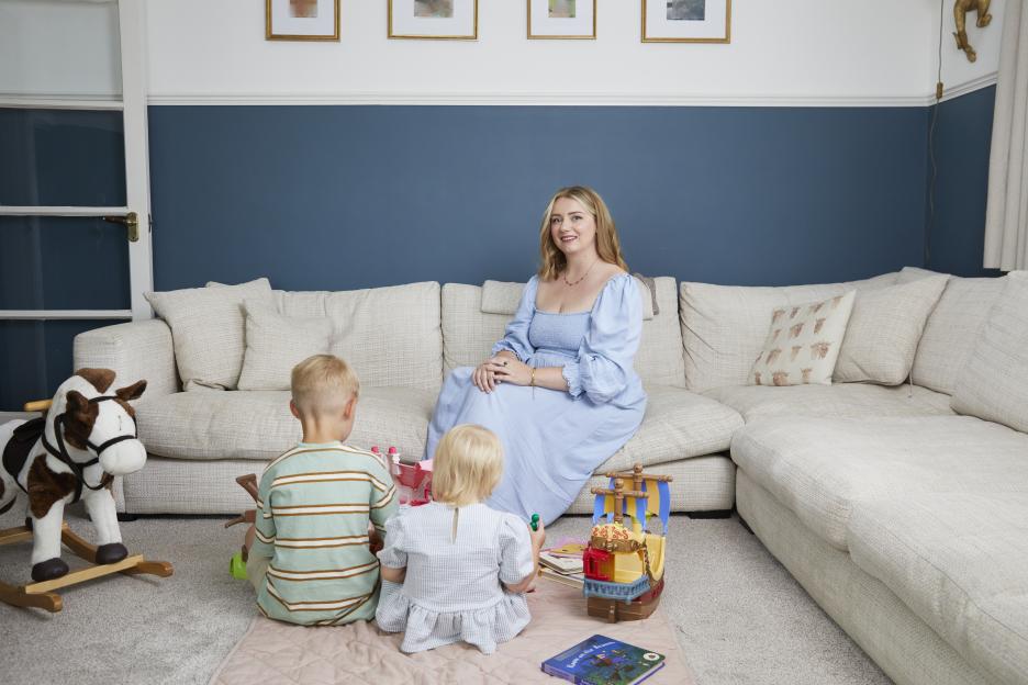Woman sitting on a couch with two young children playing on the floor.