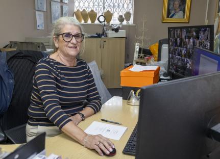 A woman sits at a desk in an office, smiling at the camera.