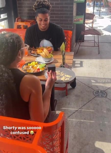 A man proposing to a woman at an outdoor restaurant.