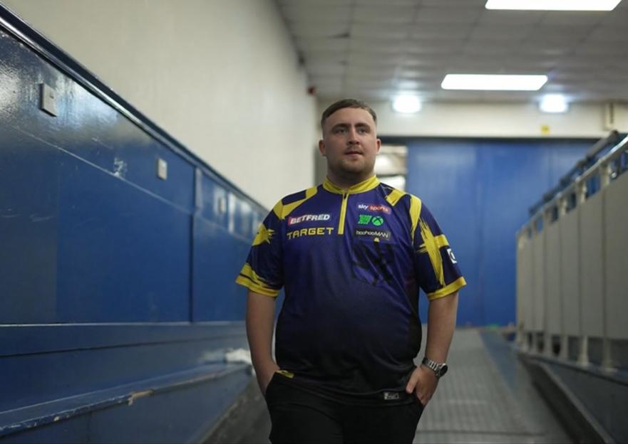 Man in darts jersey walking down a hallway.