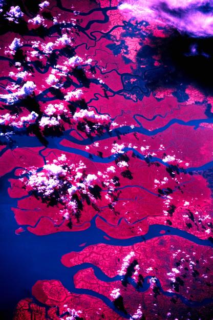 Aerial view of pink land with blue waterways and white clouds.